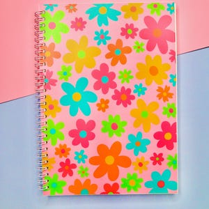 May include: A pink spiral notebook with a colourful floral pattern. The flowers are in shades of pink, blue, yellow, green, and orange.