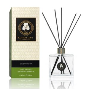May include: A clear glass bottle with black reeds and a white label. The label has a gold border and a small image of a dog. The text on the label reads "Grapefruit & Mint", "Reed Diffuser", "Diffuseur de Parfum", "6.5 fl oz e 192 mL", "RAINIER'S GIFTS", "CELEBRATE LIFE", and "RG".