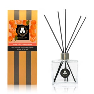 May include: A glass bottle reed diffuser with black reeds and a gold cap. The bottle is filled with a clear liquid and has a label that says "Moroccan Tangerine" and "Rainier's Gifts Celebrate Life". The label also includes a small image of a poodle. The bottle is sitting on a white background.