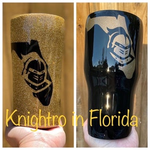 Puede incluir: Dos vasos t&eacute;rmicos con acabado de purpurina dorada y un dise&ntilde;o de casco de caballero negro. Los vasos est&aacute;n decorados con el contorno del estado de Florida. El texto "Knightro in Florida" es visible en la parte inferior de la imagen.