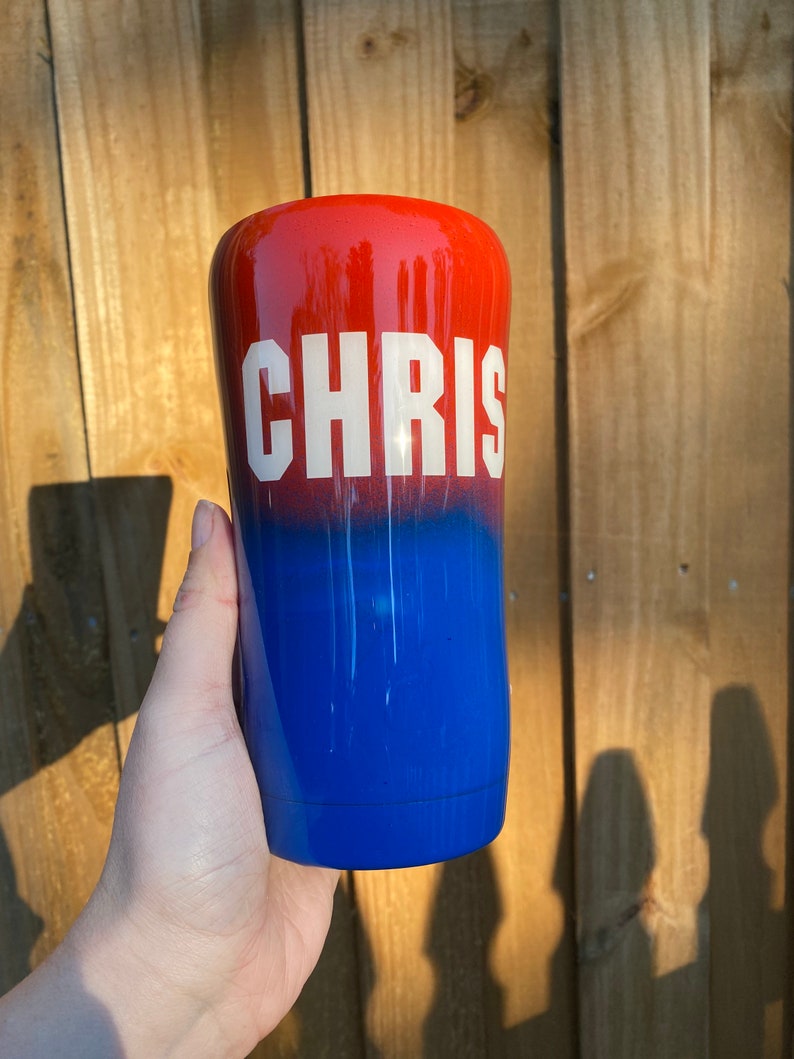 May include: A red and blue ombre tumbler with the name "CHRIS" in white lettering.