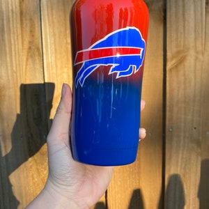 May include: A red and blue ombre tumbler with a white Buffalo Bills logo. The tumbler is made of stainless steel and has a double-walled design.
