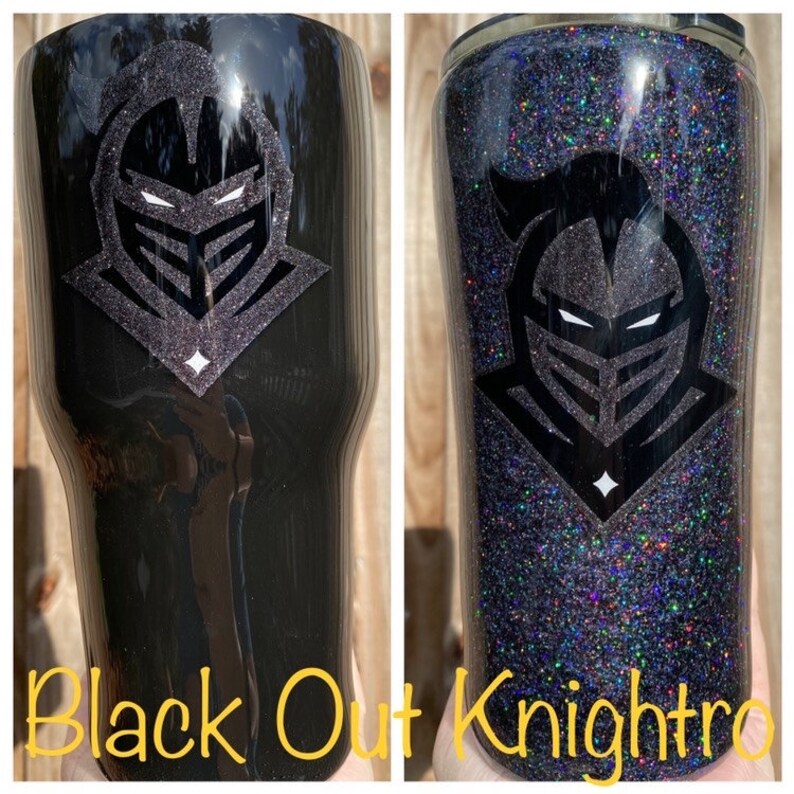 Puede incluir: Dos vasos negros con un dise&ntilde;o de casco de caballero. Un vaso es negro liso, el otro est&aacute; cubierto de purpurina negra. El texto "Black Out Knightro" est&aacute; en la parte inferior de la imagen.