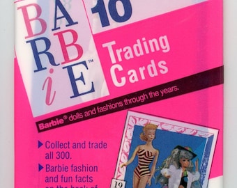 May include: Sealed pack of Barbie trading cards. The packaging is white and pink, with the Barbie logo and the text "Trading Cards." The pack includes images of Barbie dolls and the text "Collect and trade all 300."