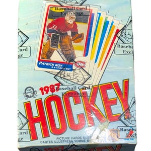 Puede incluir: Una caja sellada de cromos de hockey de 1987. La caja presenta una tarjeta de portero de hockey con el nombre de Patrick Roy. La caja tiene las palabras "Hockey" y "Baseball Card Exchange" impresas.