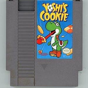 Pode incluir: Um cartucho de jogo cinza do Nintendo Entertainment System (NES) com o jogo "Yoshi's Cookie". O rótulo azul mostra o título em amarelo e um personagem Yoshi verde. A imagem mostra Yoshi com um biscoito.