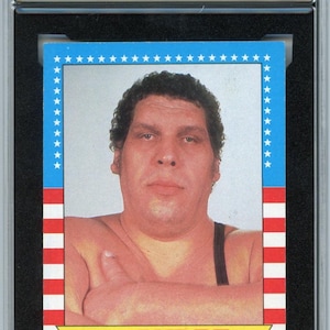 Könnte beinhalten: Eine bewertete 1987 Topps WWF-Sammelkarte mit Andre the Giant. Die Karte hat einen blauen Rand mit weißen Sternen und rot-weißen Streifen. Die Karte ist von KSA mit 6,5 bewertet. Der Text der Karte lautet "Andre the Giant".