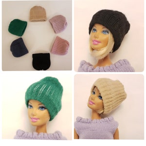 Könnte beinhalten: Ein Set mit zehn bunten Strickmützen für Puppen. Die Mützen sind in verschiedenen Farben, darunter Schwarz, Grün, Rosa und Beige. Die Mützen werden auf dem Kopf einer Puppe gezeigt und auf einer weißen Oberfläche ausgelegt.