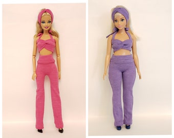 May include: Two dolls wearing matching outfits. The doll on the left is wearing a pink halter top and pants. The doll on the right is wearing a purple halter top and pants. Both dolls are wearing headbands.