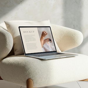 Könnte beinhalten: Ein weißer Laptop mit einem schwarzen Bildschirm, auf dem das Wort "MOCKUP" und Text über die Website Big Cartel angezeigt werden. Der Laptop steht auf einem weißen, flauschigen Stuhl.