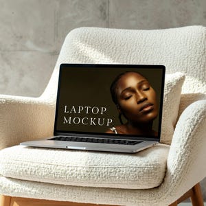 Könnte beinhalten: Ein silberner Laptop mit einem schwarzen Bildschirm, auf dem das Gesicht einer Frau und der Text "LAPTOP MOCKUP" zu sehen sind. Der Laptop steht auf einem weißen Sessel.