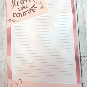 May include: A lined notepad with a pink and white design. The notepad features the text "Let your Heart take Courage" and "Psalm 31:24" in a decorative font. The notepad has a torn paper effect and heart accents.