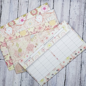 May include: Floral patterned budget envelopes and planner inserts. The envelopes feature a light pink, cream, and green floral design. The planner insert has a grid for tracking expenses and the text "Amount per Paycheck" and "Sinking Fund".