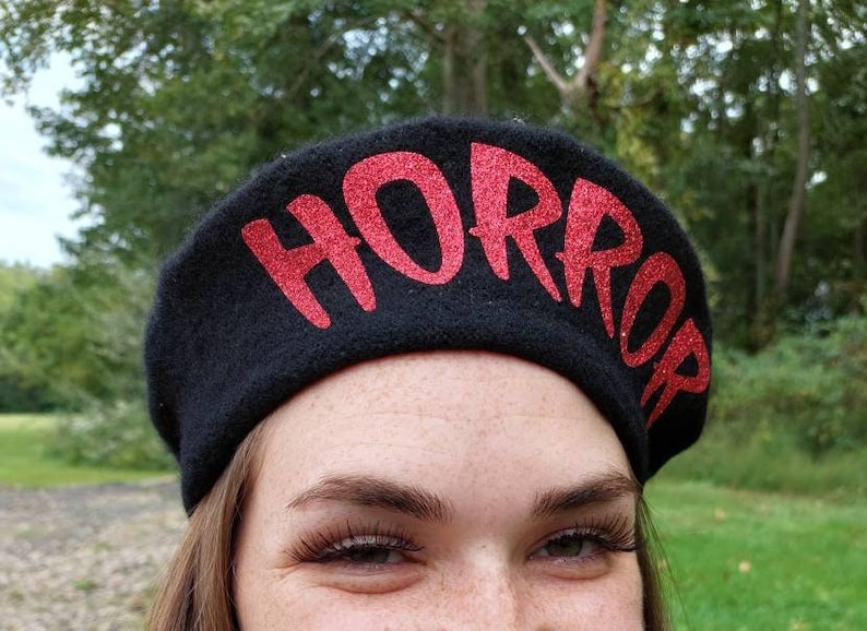 K&ouml;nnte beinhalten: Eine schwarze Baskenm&uuml;tze mit dem Wort "HORROR" in roten Glitzer geschrieben.