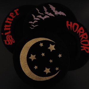 K&ouml;nnte beinhalten: Drei schwarze Filzkreise mit Glitzerdesigns. Der erste Kreis hat das Wort "Sinner" in rotem Glitzer. Der zweite Kreis hat einen goldenen Glitzer-Halbmond mit Sternen. Der dritte Kreis hat das Wort "Horror" in rotem Glitzer.