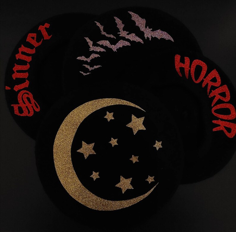 K&ouml;nnte beinhalten: Drei schwarze Filzkreise mit Glitzerdesigns. Der erste Kreis hat das Wort "Sinner" in rotem Glitzer. Der zweite Kreis hat einen goldenen Glitzer-Halbmond mit Sternen. Der dritte Kreis hat das Wort "Horror" in rotem Glitzer.