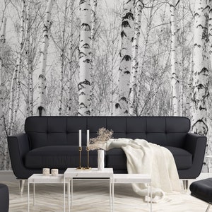 May include: A black leather sofa with a white throw blanket sits in front of a wall with a black and white birch tree wallpaper. Three white marble coffee tables are in front of the sofa.
