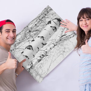 May include: A couple smiling and giving thumbs up while holding a black and white print of birch trees.