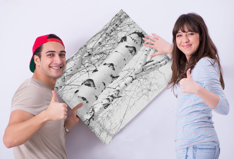 May include: A couple smiling and giving thumbs up while holding a black and white print of birch trees.