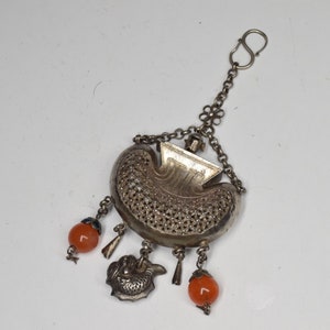 Op de afbeelding: Een zilveren bedel met een filigraanontwerp, in de vorm van een halve maan, met een ketting en een haak. De bedel heeft drie hangende oranje kralen en een zilveren visbedel.
