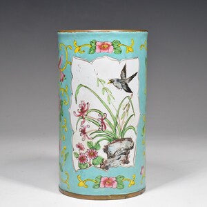 May include: A cylindrical blue and white enamelware vase with a floral and bird design. The vase has a gold rim and base.