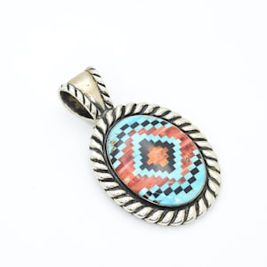 May include: Silver-tone oval pendant with a rope-style border and bail. The pendant has a mosaic design with turquoise, red, black, and orange geometric shapes. The pendant is set against a white background.