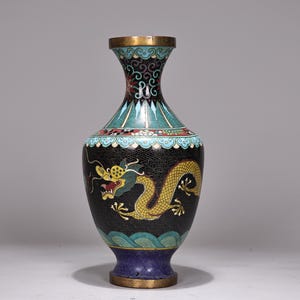 May include: An antique vase with a black background and a golden dragon design. The vase has a flared top with teal, red, and gold accents. The base is a deep blue colour, and the vase is approximately 25 cm tall.