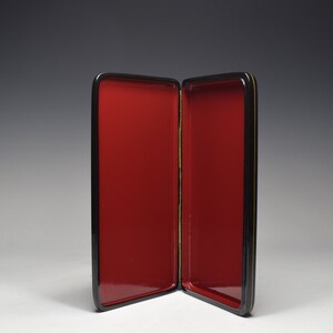 May include: A black lacquered box with a red interior. The box is open and the interior is visible. The box is made of wood and has a gold trim.