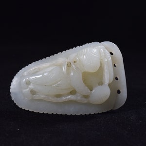 May include: A carved white jade sculpture depicting a reclining figure. The sculpture has intricate details, including the figure's facial features and clothing. The jade is smooth and polished, with a slight translucence. The sculpture is set against a black background.