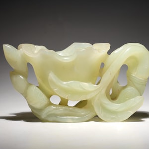 May include: A pale green jade carving of a stylized flower with a hollow center. The carving is intricately detailed and has a smooth, polished finish.