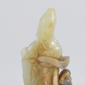 Puede incluir: Una escultura de jade blanco de una mujer sosteniendo a un ni&ntilde;o. La escultura est&aacute; tallada en un estilo chino tradicional.