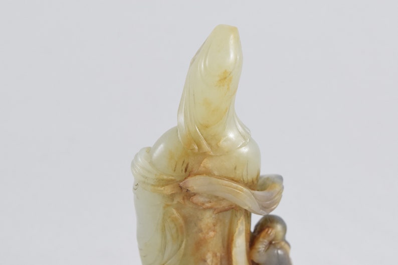 Puede incluir: Una escultura de jade blanco de una mujer sosteniendo a un ni&ntilde;o. La escultura est&aacute; tallada en un estilo chino tradicional.