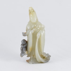 Puede incluir: Una escultura de jade blanco de una figura femenina con un ni&ntilde;o a su lado. La figura lleva una t&uacute;nica larga y una corona en la cabeza. La escultura est&aacute; tallada con un estilo detallado e intrincado.