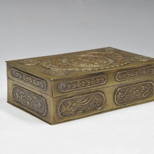 May include: A rectangular brass box with intricate engraved designs. The box features a raised circular design on the top and a repeating pattern of dragons and floral motifs on the sides.