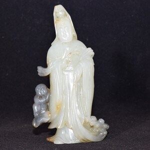 Puede incluir: Una escultura de jade blanco de una figura femenina de pie con un ni&ntilde;o a su lado. La figura lleva una t&uacute;nica larga y tiene una expresi&oacute;n serena. La escultura est&aacute; tallada y pulida de forma intrincada.