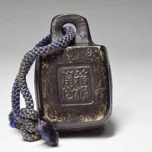 May include: A small, dark brown, rectangular weight with a loop at the top. The weight has a square inscription in Chinese characters. A blue and gray rope is attached to the loop.