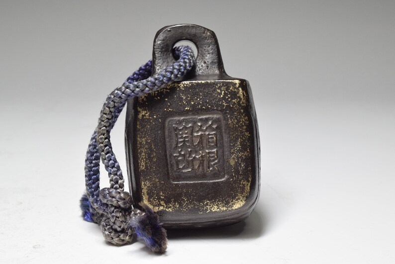 May include: A small, dark brown, rectangular weight with a loop at the top. The weight has a square inscription in Chinese characters. A blue and gray rope is attached to the loop.