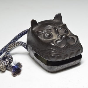 May include: A black, carved, lion-shaped bell with a gray and blue rope attached.