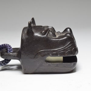May include: A black metal bell with a dragon head design. The bell has a rope attached to it.