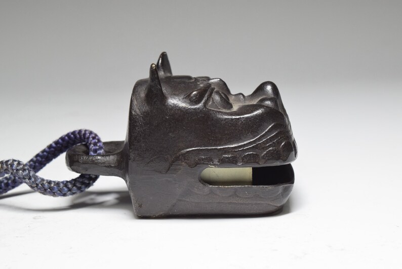 May include: A black metal bell with a dragon head design. The bell has a rope attached to it.