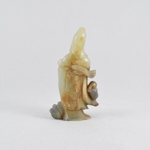 Puede incluir: Una figurita de jade tallada de una mujer que sostiene a un ni&ntilde;o. La figurita es de color amarillo p&aacute;lido con acentos marrones.