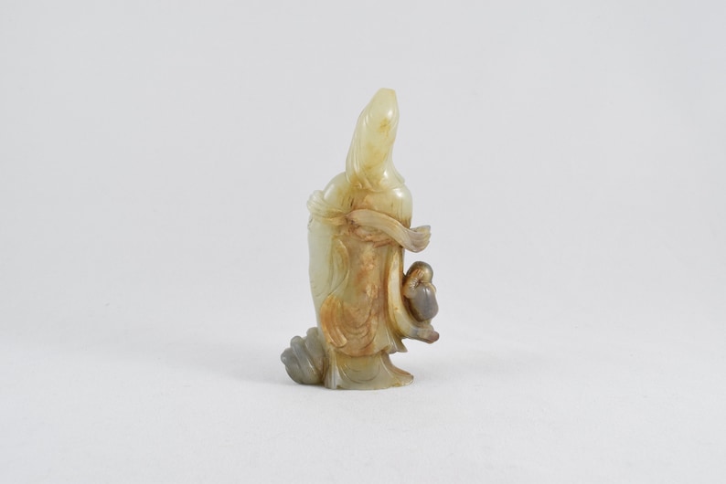 Puede incluir: Una figurita de jade tallada de una mujer que sostiene a un ni&ntilde;o. La figurita es de color amarillo p&aacute;lido con acentos marrones.