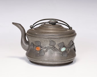 Puede incluir: Una tetera de plata con un diseño floral decorativo y acentos de piedras preciosas de colores. La tetera tiene una tapa con bisagras y un asa.