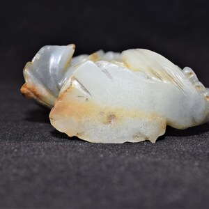 Puede incluir: Una talla de jade blanco de una criatura m&iacute;tica, posiblemente un drag&oacute;n o un f&eacute;nix. La talla es detallada e intrincada, con una forma fluida y org&aacute;nica. El jade es transl&uacute;cido y tiene un ligero tono marr&oacute;n.