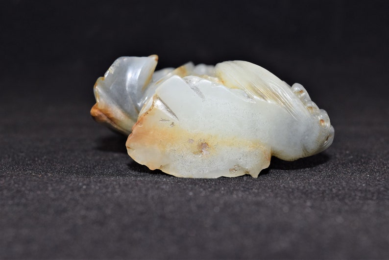 Puede incluir: Una talla de jade blanco de una criatura m&iacute;tica, posiblemente un drag&oacute;n o un f&eacute;nix. La talla es detallada e intrincada, con una forma fluida y org&aacute;nica. El jade es transl&uacute;cido y tiene un ligero tono marr&oacute;n.