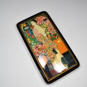 May include: A rectangular wooden box with a black lacquered finish and a colorful painted scene of a woman in a floral dress standing in a garden. The box has a gold trim around the edges.