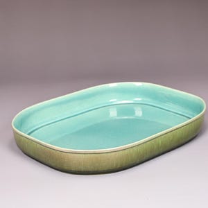 May include: A ceramic serving dish with a rounded rectangular shape. The interior is a bright turquoise color, while the exterior has a textured, olive green finish. The dish has a smooth, glossy surface and a simple, elegant design.