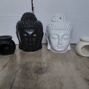 May include: Two ceramic Buddha head oil diffusers, one black and one white, with a small round black and white oil burner on each side.