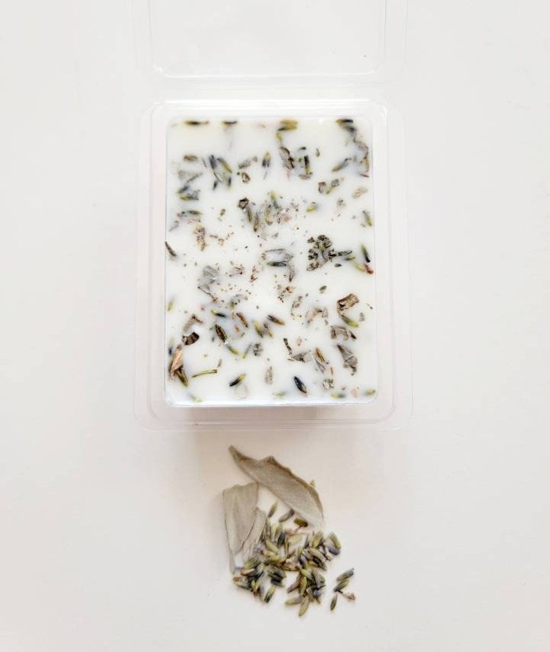 Pu&ograve; includere: Una candela bianca con erbe secche di lavanda e salvia incorporate nella cera. La candela &egrave; in un contenitore di plastica trasparente.