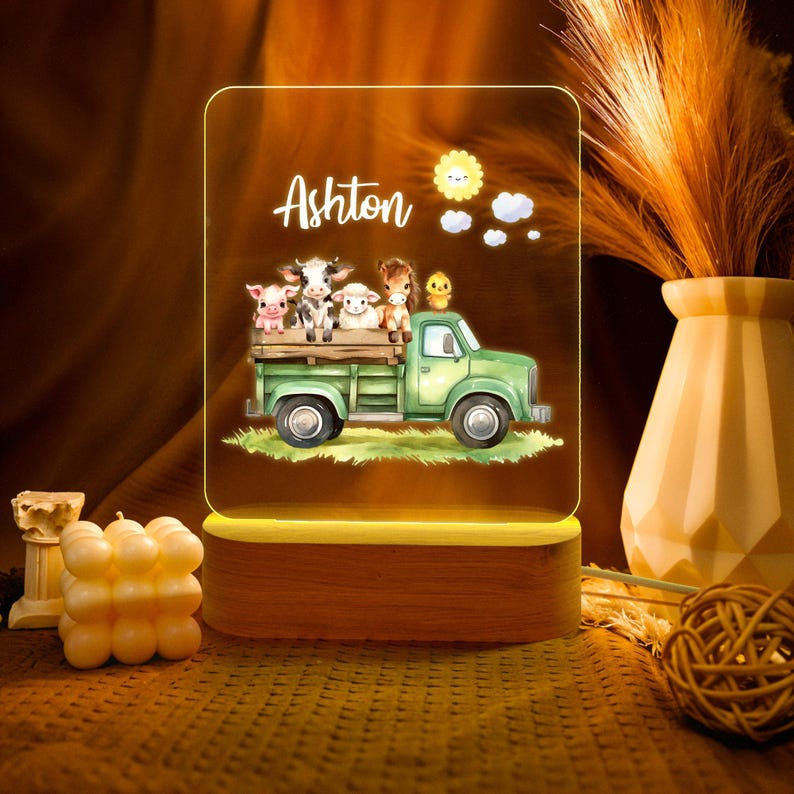 May include: A personalized night light with a wooden base and a clear acrylic panel. The panel features a green truck with a variety of farm animals, including a pig, cow, sheep, and a chick. The name "Ashton" is printed on the panel.